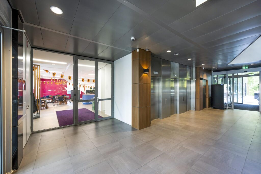 Modern lobby area at Koningin Wilhelminaplein with elevators and a view into a decorated office space.
